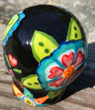 Load image into Gallery viewer, This hand-painted ceramic skull art is an homage to the traditional Mexican Day of the Dead. The inspiration for the skull's exquisite detail was taken from a beautiful flower photographed at the United States Botanic Garden - a whimsical surprise of small flowers floating in water. Bring La Muerte Calavera de Ofrenda, or 'skull of offering', into your home for a captivating reminder of Mexican tradition. H 2 3/4” x W 2” x D 2”