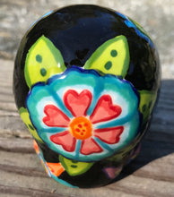 Load image into Gallery viewer, This hand-painted ceramic skull art is an homage to the traditional Mexican Day of the Dead. The inspiration for the skull's exquisite detail was taken from a beautiful flower photographed at the United States Botanic Garden - a whimsical surprise of small flowers floating in water. Bring La Muerte Calavera de Ofrenda, or 'skull of offering', into your home for a captivating reminder of Mexican tradition. H 2 3/4” x W 2” x D 2”