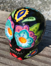 Load image into Gallery viewer, This black ceramic sugar skull, inspired by nature, is adorned with hand-painted floral motifs, hearts, leaves and colorful accents. Its vibrant style and intricate details create a stunning Dia De Los Muertos calavera. Perfect for creating ofrendas to celebrate the Day of the Dead. Measurements: H 2 3/4” x W 2” x D 2”