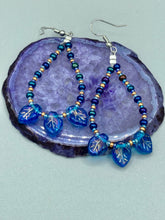 Load image into Gallery viewer, These striking Royal Blue Pressed Glass Leaf Beaded Hoop Earrings feature a shimmery finish with a hint of gold, purple, blue and pink. Gold, dark and light blue glass beads complete the piece. Measurements: 2 1/2" length