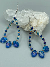 Load image into Gallery viewer, These striking Royal Blue Pressed Glass Leaf Beaded Hoop Earrings feature a shimmery finish with a hint of gold, purple, blue and pink. Gold, dark and light blue glass beads complete the piece. Measurements: 2 1/2" length