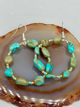 Load image into Gallery viewer, Our Blue-Green Magnesite Stone Beaded Hoop Earrings provide a nature-inspired look that is perfect for any boho-chic style. These earrings feature natural magnesite stone beads with small beads of turquoise and gold glass for subtle accent. Show off your bohemian look with these eye-catching hoops. Measurements: 2" length