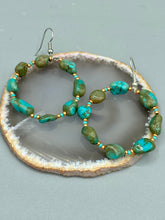 Load image into Gallery viewer, Our Blue-Green Magnesite Stone Beaded Hoop Earrings provide a nature-inspired look that is perfect for any boho-chic style. These earrings feature natural magnesite stone beads with small beads of turquoise and gold glass for subtle accent. Show off your bohemian look with these eye-catching hoops. Measurements: 2" length