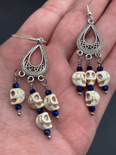 Load image into Gallery viewer, Stunning Cascade of Tiny Howlite Skull Dark Purple Glass Bead Chandelier Earrings. Chicana Chingona Chola Style Jewelry. Beautiful elegant set of teardrop earrings has an eerie beautiful vibe. Tiny dangling howlite skull beads. You can dress these up or down, it will definitely give your outfit a unique look. Versatile looks from Witchy, Goth, Dia De Los Muertos, Vampire Goth. Measurements: 2” in length