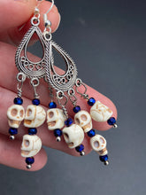 Load image into Gallery viewer, Stunning Cascade of Tiny Howlite Skull Dark Purple Glass Bead Chandelier Earrings. Chicana Chingona Chola Style Jewelry. Beautiful elegant set of teardrop earrings has an eerie beautiful vibe. Tiny dangling howlite skull beads. You can dress these up or down, it will definitely give your outfit a unique look. Versatile looks from Witchy, Goth, Dia De Los Muertos, Vampire Goth. Measurements: 2” in length