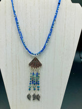 Load image into Gallery viewer, Triangle Illuminati Silver Plated Pendant With Blue And Silver Color Glass Bead Adjustable Necklace.  Mysterious and unique necklace has a very whimsical vibe with a dash of mystery. Contains 5 beaded strands with intricate leaf charms that create movement. This unique look will complete any outfit. Witchy, Gothic, Illuminati, Mysterious versatile style, bold elegant piece of jewelry.  Measurements: Necklace is 16 1/2” adjustable up to 19" in length - pendant is 4” Height with bail