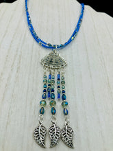 Load image into Gallery viewer, Triangle Illuminati Silver Plated Pendant With Blue And Silver Color Glass Bead Adjustable Necklace.  Mysterious and unique necklace has a very whimsical vibe with a dash of mystery. Contains 5 beaded strands with intricate leaf charms that create movement. This unique look will complete any outfit. Witchy, Gothic, Illuminati, Mysterious versatile style, bold elegant piece of jewelry.  Measurements: Necklace is 16 1/2” adjustable up to 19" in length - pendant is 4” Height with bail