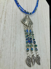 Load image into Gallery viewer, Triangle Illuminati Silver Plated Pendant With Blue And Silver Color Glass Bead Adjustable Necklace.  Mysterious and unique necklace has a very whimsical vibe with a dash of mystery. Contains 5 beaded strands with intricate leaf charms that create movement. This unique look will complete any outfit. Witchy, Gothic, Illuminati, Mysterious versatile style, bold elegant piece of jewelry.  Measurements: Necklace is 16 1/2” adjustable up to 19" in length - pendant is 4” Height with bail