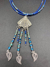 Load image into Gallery viewer, Triangle Illuminati Silver Plated Pendant With Blue And Silver Color Glass Bead Adjustable Necklace.  Mysterious and unique necklace has a very whimsical vibe with a dash of mystery. Contains 5 beaded strands with intricate leaf charms that create movement. This unique look will complete any outfit. Witchy, Gothic, Illuminati, Mysterious versatile style, bold elegant piece of jewelry.  Measurements: Necklace is 16 1/2” adjustable up to 19" in length - pendant is 4” Height with bail