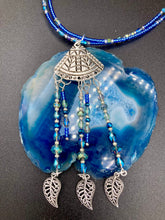 Load image into Gallery viewer, Triangle Illuminati Silver Plated Pendant With Blue And Silver Color Glass Bead Adjustable Necklace.  Mysterious and unique necklace has a very whimsical vibe with a dash of mystery. Contains 5 beaded strands with intricate leaf charms that create movement. This unique look will complete any outfit. Witchy, Gothic, Illuminati, Mysterious versatile style, bold elegant piece of jewelry.  Measurements: Necklace is 16 1/2” adjustable up to 19" in length - pendant is 4” Height with bail