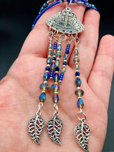Load image into Gallery viewer, Triangle Illuminati Silver Plated Pendant With Blue And Silver Color Glass Bead Adjustable Necklace.  Mysterious and unique necklace has a very whimsical vibe with a dash of mystery. Contains 5 beaded strands with intricate leaf charms that create movement. This unique look will complete any outfit. Witchy, Gothic, Illuminati, Mysterious versatile style, bold elegant piece of jewelry.  Measurements: Necklace is 16 1/2” adjustable up to 19" in length - pendant is 4” Height with bail