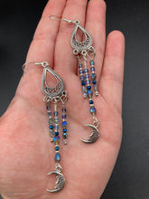 Load image into Gallery viewer, These three-strand chandelier style earrings offer an ornate and eye-catching look with their whimsical blue celestial charm accents adorned with smiling crescent moon designs. Perfect for creating a fairy princess, witchy, or boho aesthetic, they provide plenty of movement and can easily be added to any jewelry collection. Measurements: 3 1/2” in length