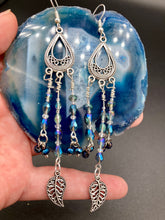 Load image into Gallery viewer, Blue Moroccan Inspired Large Chandelier Earrings. Three strands of beautiful blue and iridescent glass beads with intricate silver plated leaf charms create a lot of movement. Versatile, perfect for whimsical fairy princes, good witch, hippie nature lovers looks. These earring will compliment any look. Measurements: 3 1/2” in length