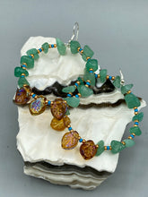 Load image into Gallery viewer, These Aventurine Stone Chip Beaded Hoop Earrings feature natural aventurine stone chips, turquoise, and gold glass beads. The amber-tone pressed glass leaf charm has an iridescent shimmer finish, with subtle accents of gold, purple, blue, and pink. Measurements: 2" length