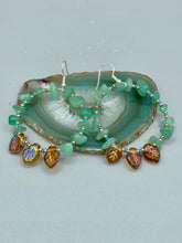 Load image into Gallery viewer, These Aventurine Stone Chip Beaded Hoop Earrings feature natural aventurine stone chips, turquoise, and gold glass beads. The amber-tone pressed glass leaf charm has an iridescent shimmer finish, with subtle accents of gold, purple, blue, and pink. Measurements: 2" length