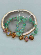 Load image into Gallery viewer, These Aventurine Stone Chip Beaded Hoop Earrings feature natural aventurine stone chips, turquoise, and gold glass beads. The amber-tone pressed glass leaf charm has an iridescent shimmer finish, with subtle accents of gold, purple, blue, and pink. Measurements: 2" length