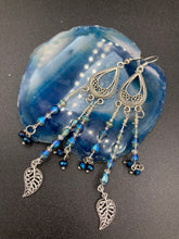 Load image into Gallery viewer, Blue Moroccan Inspired Large Chandelier Earrings. Three strands of beautiful blue and iridescent glass beads with intricate silver plated leaf charms create a lot of movement. Versatile, perfect for whimsical fairy princes, good witch, hippie nature lovers looks. These earring will compliment any look. Measurements: 3 1/2” in length
