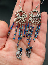Load image into Gallery viewer, These intricate moroccan blue Inspired large chandelier earrings boast five strands of blue and iridescent glass beads of various hues, including silver and gold. Additionally, two small dark blue glass beads with a silver leaf add a touch of dimension and motion. The perfect addition to any Fairy Princess or whimsical aesthetic.  Measurements: 4” in length