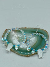Load image into Gallery viewer, This stylish set of earrings feature milky white fish-shaped glass beads, complemented by light blue and iridescent teardrop glass beads. The fish-shaped glass beads feature intricate details, including fins and an eye. Measurements: 1 7/8” in length