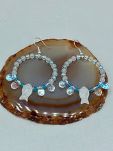 Load image into Gallery viewer, This stylish set of earrings feature milky white fish-shaped glass beads, complemented by light blue and iridescent teardrop glass beads. The fish-shaped glass beads feature intricate details, including fins and an eye. Measurements: 1 7/8” in length
