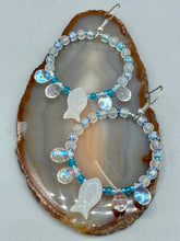 Load image into Gallery viewer, This stylish set of earrings feature milky white fish-shaped glass beads, complemented by light blue and iridescent teardrop glass beads. The fish-shaped glass beads feature intricate details, including fins and an eye. Measurements: 1 7/8” in length