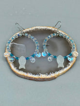 Load image into Gallery viewer, This stylish set of earrings feature milky white fish-shaped glass beads, complemented by light blue and iridescent teardrop glass beads. The fish-shaped glass beads feature intricate details, including fins and an eye. Measurements: 1 7/8” in length
