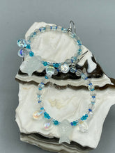 Load image into Gallery viewer, This stylish set of earrings feature milky white fish-shaped glass beads, complemented by light blue and iridescent teardrop glass beads. The fish-shaped glass beads feature intricate details, including fins and an eye. Measurements: 1 7/8” in length