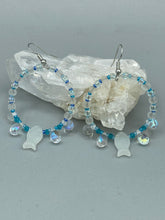 Load image into Gallery viewer, This stylish set of earrings feature milky white fish-shaped glass beads, complemented by light blue and iridescent teardrop glass beads. The fish-shaped glass beads feature intricate details, including fins and an eye. Measurements: 1 7/8” in length