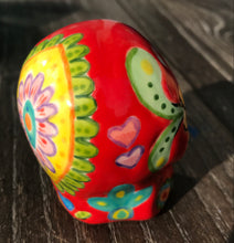 Load image into Gallery viewer, This ceramic skull statuette is a stunning piece of art inspired by nature. Its vibrant red hue is decorated with multi-color floral motifs, hearts, leaves and colorful accents, creating a beautiful piece of hand-painted, Day of the Dead-themed art. Measurements: H 2 3/4” x W 2” x D 2”