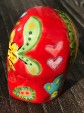 Load image into Gallery viewer, This ceramic skull statuette is a stunning piece of art inspired by nature. Its vibrant red hue is decorated with multi-color floral motifs, hearts, leaves and colorful accents, creating a beautiful piece of hand-painted, Day of the Dead-themed art. Measurements: H 2 3/4” x W 2” x D 2”