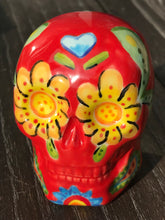 Load image into Gallery viewer, This ceramic skull statuette is a stunning piece of art inspired by nature. Its vibrant red hue is decorated with multi-color floral motifs, hearts, leaves and colorful accents, creating a beautiful piece of hand-painted, Day of the Dead-themed art. Measurements: H 2 3/4” x W 2” x D 2”