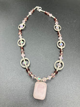 Load image into Gallery viewer, This exquisite necklace features a soft pink Rose Quartz pendant with multi-colored glass beads that transition from iridescent pink, to light purple and darker shades of purple. The sequence of beads complements the Rose Quartz pendant's delicate hue, and is accompanied with a set of subtly-styled matching earrings for a complete look. Measurements: Necklace is 16 1/2”