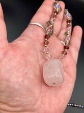 Load image into Gallery viewer, This exquisite necklace features a soft pink Rose Quartz pendant with multi-colored glass beads that transition from iridescent pink, to light purple and darker shades of purple. The sequence of beads complements the Rose Quartz pendant's delicate hue, and is accompanied with a set of subtly-styled matching earrings for a complete look. Measurements: Necklace is 16 1/2”