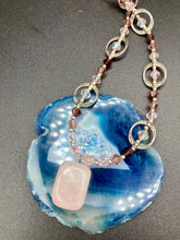 Load image into Gallery viewer, This exquisite necklace features a soft pink Rose Quartz pendant with multi-colored glass beads that transition from iridescent pink, to light purple and darker shades of purple. The sequence of beads complements the Rose Quartz pendant's delicate hue, and is accompanied with a set of subtly-styled matching earrings for a complete look. Measurements: Necklace is 16 1/2”