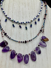 Load image into Gallery viewer, The Genuine Amethyst Natural Gemstone Adjustable Chocker Style Glass Beaded Necklace features vibrant violet and white tones. Its unique draped beading creates a beautiful style with a series of short strands of glass beads for movement and a longer strand with a multitude of amethyst nugget beads. The collar necklace hangs gracefully along the neck and chest, making it a dream come true for violet lovers.  Measurements:  Necklace is 15” in length adjustable to 18" in length