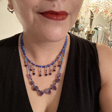 Load image into Gallery viewer, This exceptional amethyst choker-style necklace is a one-of-a-kind jewelry piece. Three beaded strands, created with varying sizes, shapes and colors of glass beads, are featured: two short strands with primarily purple beads, featuring subtle hints of blue, pink and gold; and one long strand featuring a majority of amethyst nugget beads. When worn, this necklace gracefully drapes across the neck and chest for an eye-catching display.