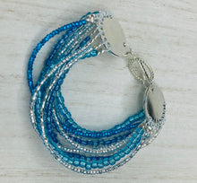 Load image into Gallery viewer, This bracelet is a chic, minimalistic design with nine beaded strands that feature various blue and silver glass beads. It measures 7 1/2" in length and has been crafted with inspiration from the ocean blue waves.