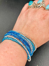 Load image into Gallery viewer, This bracelet is a chic, minimalistic design with nine beaded strands that feature various blue and silver glass beads. It measures 7 1/2" in length and has been crafted with inspiration from the ocean blue waves.