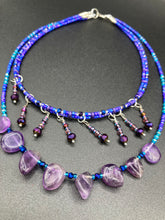 Load image into Gallery viewer, Three beaded strands using a wide range of size, shape, and color glass beads. The first two shorter stands are primarily purple glass beads that have tiny shimmery hues of blue, pink and gold. I added a series of dangling glass beads along this necklace to give this collar some movement and make it stand out even more. The third and longer strand contains a large amount of amethyst nugget beads. Large necklace hangs beautifully across your neck and chest. Necklace is 16” in adjustable up to 18" in