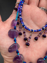 Load image into Gallery viewer, This exceptional amethyst choker-style necklace is a one-of-a-kind jewelry piece. Three beaded strands, created with varying sizes, shapes and colors of glass beads, are featured: two short strands with primarily purple beads, featuring subtle hints of blue, pink and gold; and one long strand featuring a majority of amethyst nugget beads. When worn, this necklace gracefully drapes across the neck and chest for an eye-catching display.