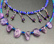 Load image into Gallery viewer, Three beaded strands using a wide range of size, shape, and color glass beads. The first two shorter stands are primarily purple glass beads that have tiny shimmery hues of blue, pink and gold. I added a series of dangling glass beads along this necklace to give this collar some movement and make it stand out even more. The third and longer strand contains a large amount of amethyst nugget beads. Large necklace hangs beautifully across your neck and chest. Necklace is 16” in adjustable up to 18" in