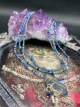 Load image into Gallery viewer, This jewelry piece is a delicate harmony of light and dark tones. Three strands feature a mix of navy blue, pewter, and oval-shaped, light blue-gray beads with a subtle iridescence of amethyst, emerald, and gold. Its celestial theme and bold composition create an alluringly elegant accessory. This whimsical necklace boasts a wonderfully unique aesthetic, featuring a wired blue luster nugget and a whimsical crescent moon charm. Measurements: Necklace is 15 1/4”adjustable up to 18"
