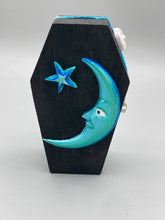 Load image into Gallery viewer, This sleek black box has an eye-catching turquoise crescent at its center, accompanied by a bright blue ribbon and a dainty white moon. Inside, the interior is decorated with a vivid royal blue and detailed with a small crescent moon and black-and-silver cross. Coffin Dimensions: Length: 4 1/2 Inches; Width: 2 1/2 inches; Height: 1 5/8 Inches