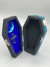 Load image into Gallery viewer, This sleek black box has an eye-catching turquoise crescent at its center, accompanied by a bright blue ribbon and a dainty white moon. Inside, the interior is decorated with a vivid royal blue and detailed with a small crescent moon and black-and-silver cross. Coffin Dimensions: Length: 4 1/2 Inches; Width: 2 1/2 inches; Height: 1 5/8 Inches
