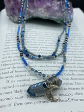 Load image into Gallery viewer, This jewelry piece is a delicate harmony of light and dark tones. Three strands feature a mix of navy blue, pewter, and oval-shaped, light blue-gray beads with a subtle iridescence of amethyst, emerald, and gold. Its celestial theme and bold composition create an alluringly elegant accessory. This whimsical necklace boasts a wonderfully unique aesthetic, featuring a wired blue luster nugget and a whimsical crescent moon charm. Measurements: Necklace is 15 1/4”adjustable up to 18"