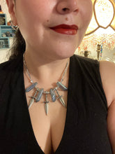 Load image into Gallery viewer, This elegant and dark necklace features shimmering light silver and gray glass beads of varying sizes and shapes for texture and dimension. The necklace is finished with blue luster crystal stone nuggets and nickel-free dagger pendants, creating a beautiful draping effect. Measurements:   Necklace is 17”adjustable up to 19"