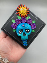 Load image into Gallery viewer, Showcasing a dark theme Frida Kahlo inspired calavera with a dark wood frame, this Day of the Dead wall decor piece is perfect for adding a traditional Mexican folk art touch to any home. Featuring an intricately detailed clay calavera in the style of Frida Kahlo, this Day of the Dead wall art decor is sure to be the centerpiece of any home décor. The calavera is wearing Frida's iconic crown of flowers, ensuring it will bring both a unique and inspiring look to any wall.