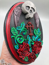 Load image into Gallery viewer, This Memento Mori Wall Art Decor is a one-of-a-kind art piece, skillfully crafted with a black polymer clay skull and wings on a dark red wood frame, decoratively woven with dark red roses and vines. It's perfect for adding an eye-catching touch to any wall and makes a unique, bold gift.  Measurements: H 7" x W 5” x D 1 1/2"