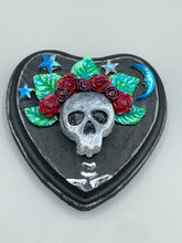 Load image into Gallery viewer, Showcasing a dark theme Frida Kahlo inspired calavera with a dark wood frame, this Day of the Dead wall decor piece is perfect for adding a traditional Mexican folk art touch to any home. Featuring an intricately detailed clay calavera in the style of Frida Kahlo, this Day of the Dead wall art decor is sure to be the centerpiece of any home décor. The calavera is wearing Frida's iconic crown of flowers, ensuring it will bring both a unique and inspiring look to any wall.