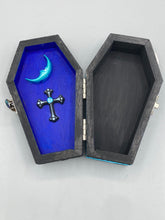 Load image into Gallery viewer, This sleek black box has an eye-catching turquoise crescent at its center, accompanied by a bright blue ribbon and a dainty white moon. Inside, the interior is decorated with a vivid royal blue and detailed with a small crescent moon and black-and-silver cross. Coffin Dimensions: Length: 4 1/2 Inches; Width: 2 1/2 inches; Height: 1 5/8 Inches